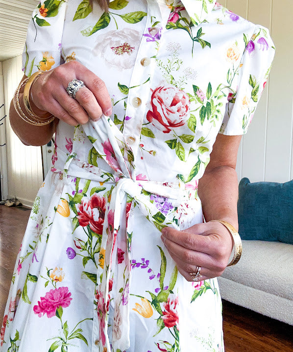 Crisp white button down shirt dress with collar, puffed short sleeves, matching belt and lined skirt featuring spring floral print.