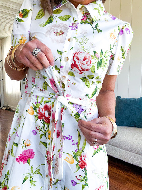 Crisp white button down shirt dress with collar, puffed short sleeves, matching belt and lined skirt featuring spring floral print.