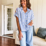 Light blue and white geometric short sleeved button down with collar and cuffed sleeves with bold orange, green and pink embroidery on the shoulders.