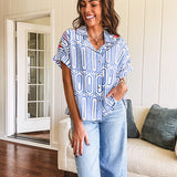 Light blue and white geometric short sleeved button down with collar and cuffed sleeves with bold orange, green and pink embroidery on the shoulders.