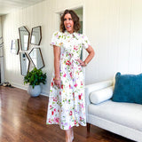 Crisp white button down shirt dress with collar, puffed short sleeves, matching belt and lined skirt featuring spring floral print.
