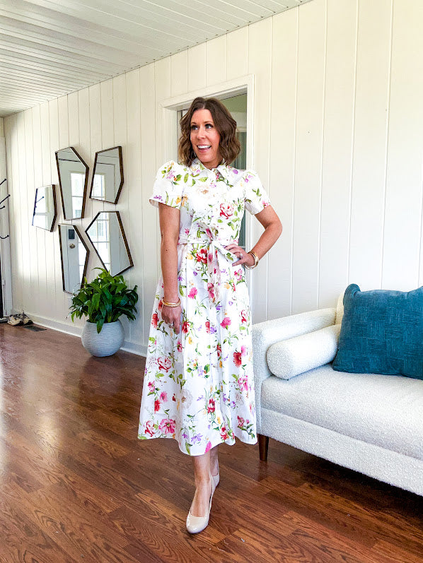 Crisp white button down shirt dress with collar, puffed short sleeves, matching belt and lined skirt featuring spring floral print.
