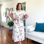 Crisp white button down shirt dress with collar, puffed short sleeves, matching belt and lined skirt featuring spring floral print.