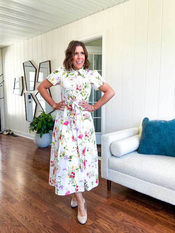 Crisp white button down shirt dress with collar, puffed short sleeves, matching belt and lined skirt featuring spring floral print.