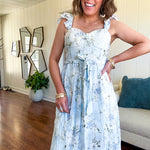 Light blue midi dress with white and green muted florals throughout featuring a bustier bodice, stretchy flutter straps, matching belt and fully lined skirt with slits.