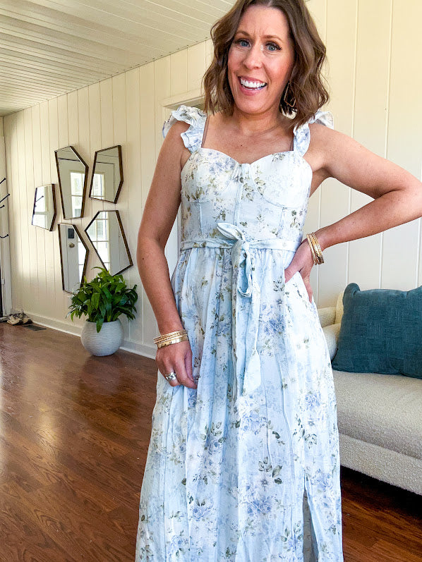Light blue midi dress with white and green muted florals throughout featuring a bustier bodice, stretchy flutter straps, matching belt and fully lined skirt with slits.