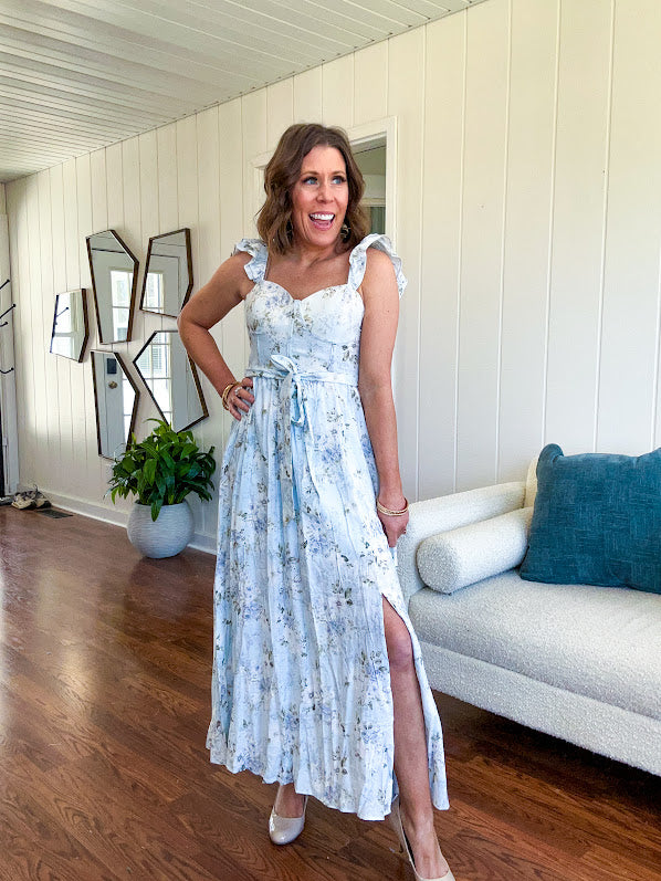 Light blue midi dress with white and green muted florals throughout featuring a bustier bodice, stretchy flutter straps, matching belt and fully lined skirt with slits.
