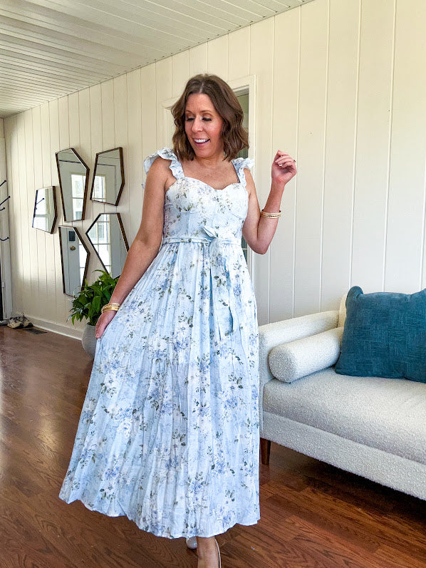 Light blue midi dress with white and green muted florals throughout featuring a bustier bodice, stretchy flutter straps, matching belt and fully lined skirt with slits.