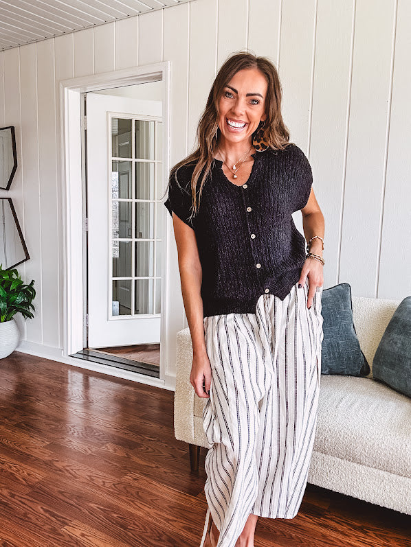 Textured black woven sweater tank with faux wooden buttons down the front and a V neck and hem.