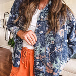 Dark navy washed denim jacket with snap button front and pastel floral print throughout.