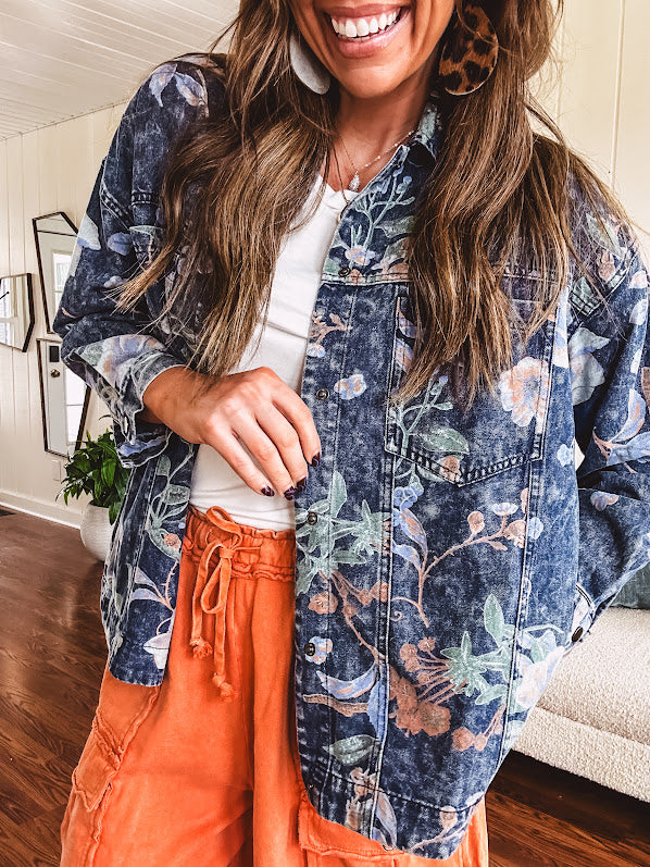 Dark navy washed denim jacket with snap button front and pastel floral print throughout.