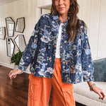 Dark navy washed denim jacket with snap button front and pastel floral print throughout.