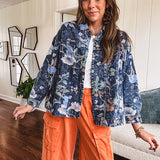 Dark navy washed denim jacket with snap button front and pastel floral print throughout.