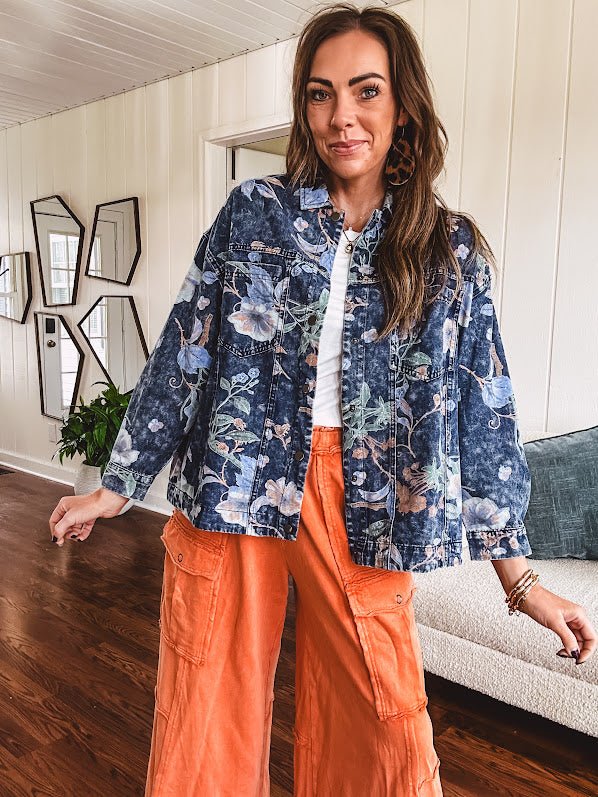 Dark navy washed denim jacket with snap button front and pastel floral print throughout.
