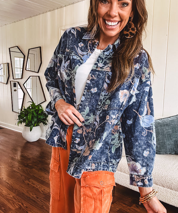 Dark navy washed denim jacket with snap button front and pastel floral print throughout.
