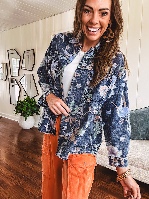Dark navy washed denim jacket with snap button front and pastel floral print throughout.