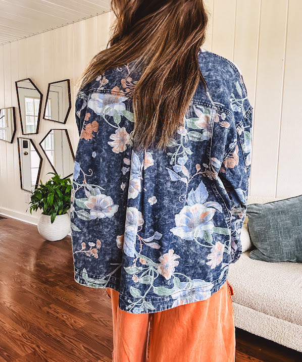 Dark navy washed denim jacket with snap button front and pastel floral print throughout.