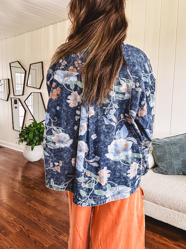 Dark navy washed denim jacket with snap button front and pastel floral print throughout.