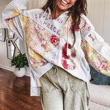 Light grey and cream hoodie with V neck, pink and yellow floral patchwork and retro graphics, split high/low hem.