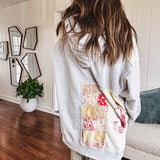 Light grey and cream hoodie with V neck, pink and yellow floral patchwork and retro graphics, split high/low hem.