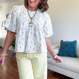 Cream textured flowy fabric with small pink florals throughout with pintuck yoke, puffed short sleeves, zip up back and wide, flowy hem.