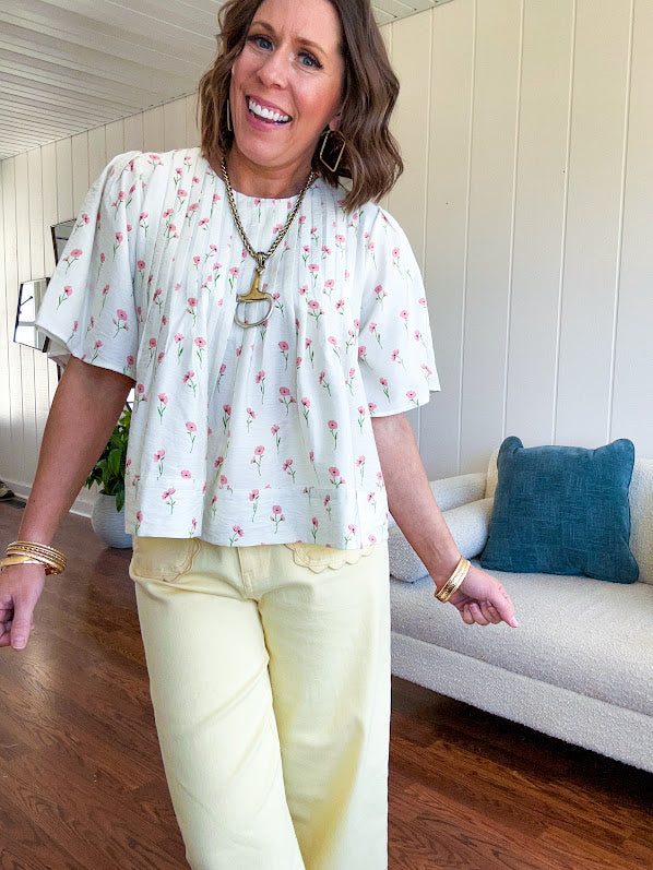 Cream textured flowy fabric with small pink florals throughout with pintuck yoke, puffed short sleeves, zip up back and wide, flowy hem.