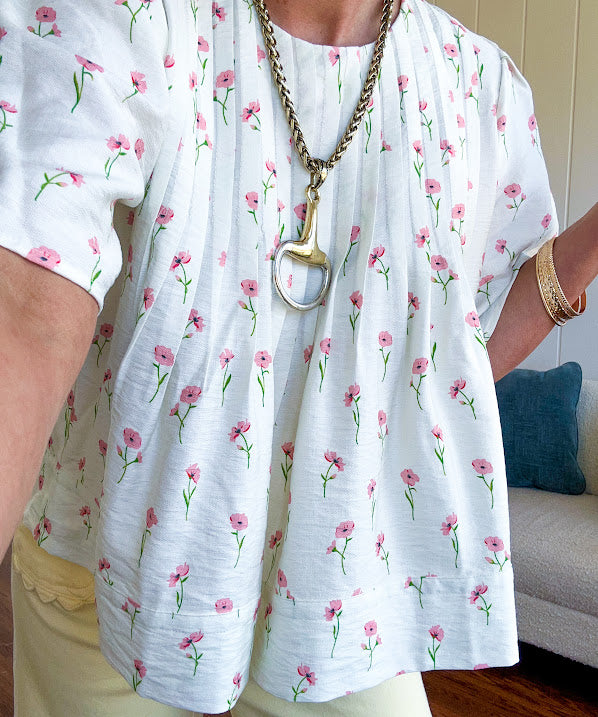 Cream textured flowy fabric with small pink florals throughout with pintuck yoke, puffed short sleeves, zip up back and wide, flowy hem.