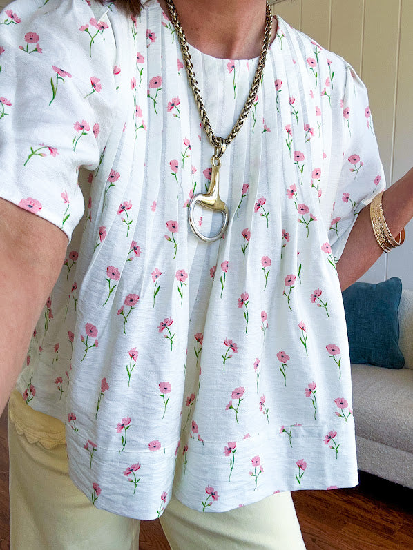Cream textured flowy fabric with small pink florals throughout with pintuck yoke, puffed short sleeves, zip up back and wide, flowy hem.