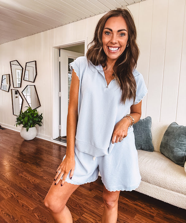 Light blue ribbed cap sleeve 1/4 zip top with matching elastic drawstring waist shorts with scalloped trim at the hem and sleeves, trimmed in white.