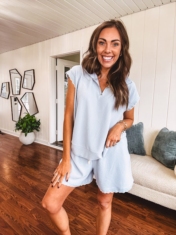 Light blue ribbed cap sleeve 1/4 zip top with matching elastic drawstring waist shorts with scalloped trim at the hem and sleeves, trimmed in white.