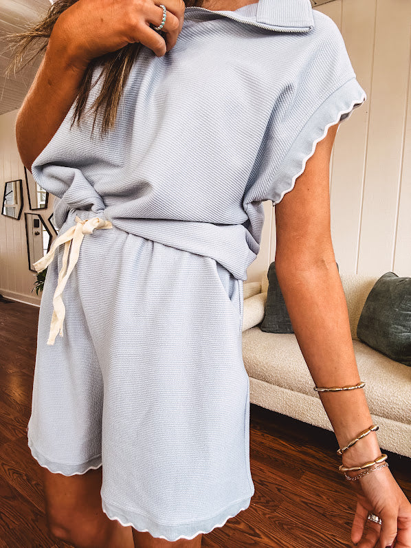 Light blue ribbed cap sleeve 1/4 zip top with matching elastic drawstring waist shorts with scalloped trim at the hem and sleeves, trimmed in white.