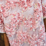 Dusty pink short dress with round neck, short sleeves, tulle overlay with fabric florals with sequined centers and lace accents with pearl trim on the sleeves.