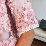 Dusty pink short dress with round neck, short sleeves, tulle overlay with fabric florals with sequined centers and lace accents with pearl trim on the sleeves.