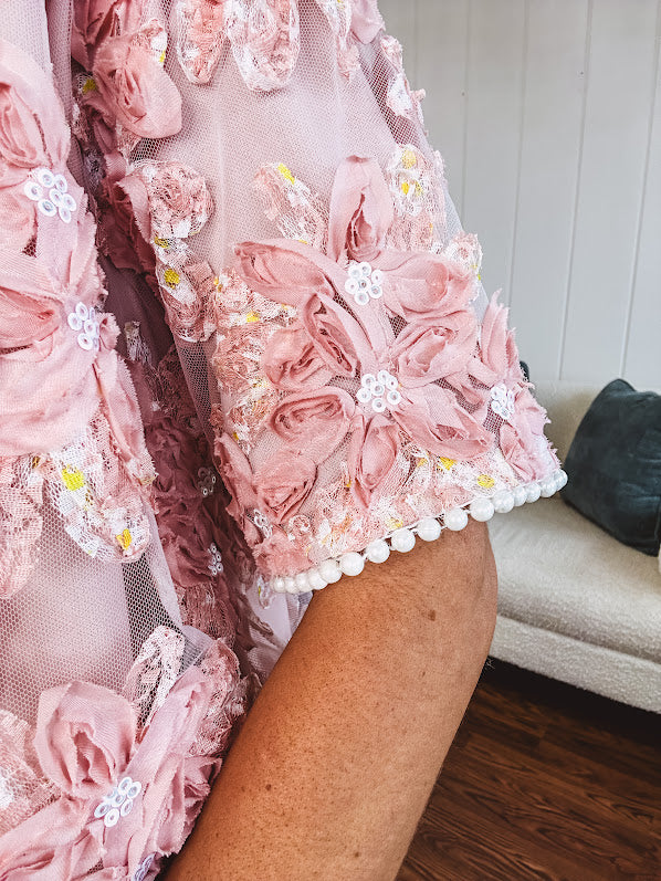 Dusty pink short dress with round neck, short sleeves, tulle overlay with fabric florals with sequined centers and lace accents with pearl trim on the sleeves.