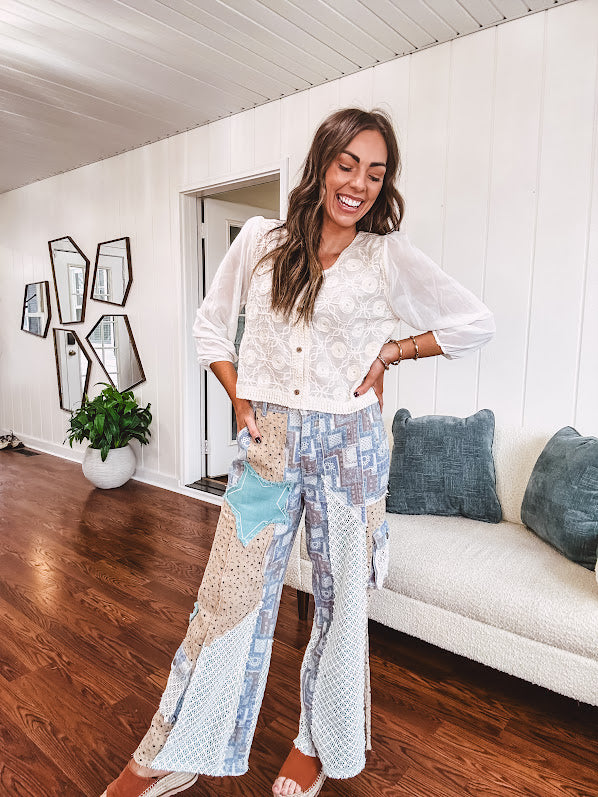 Thin, lightweight wide leg pants with elastic back button and zipper closure, teal, blue and taupe patchwork and mixed fabrics throughout with lace and star patches, pockets and raw hem.
