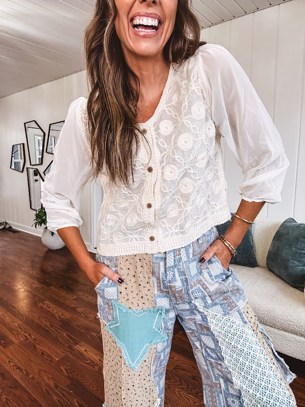 Thin, lightweight wide leg pants with elastic back button and zipper closure, teal, blue and taupe patchwork and mixed fabrics throughout with lace and star patches, pockets and raw hem.