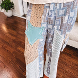 Thin, lightweight wide leg pants with elastic back button and zipper closure, teal, blue and taupe patchwork and mixed fabrics throughout with lace and star patches, pockets and raw hem.
