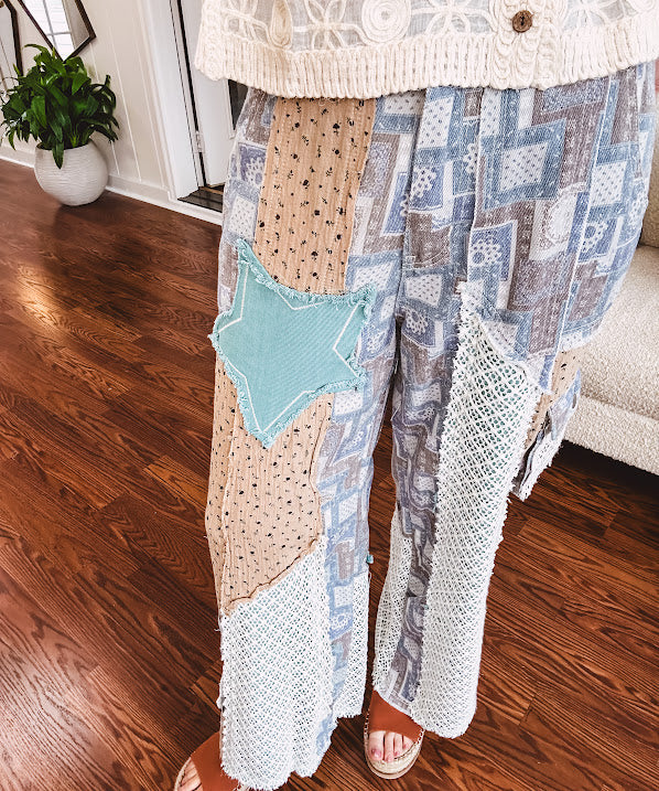 Thin, lightweight wide leg pants with elastic back button and zipper closure, teal, blue and taupe patchwork and mixed fabrics throughout with lace and star patches, pockets and raw hem.