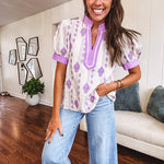 Fully lined lavender and cream blouse with lavender trim at the mock collar and V neck and cuffs, short puffed sleeves and lavender and cream embroidery throughout in an abstract pattern.