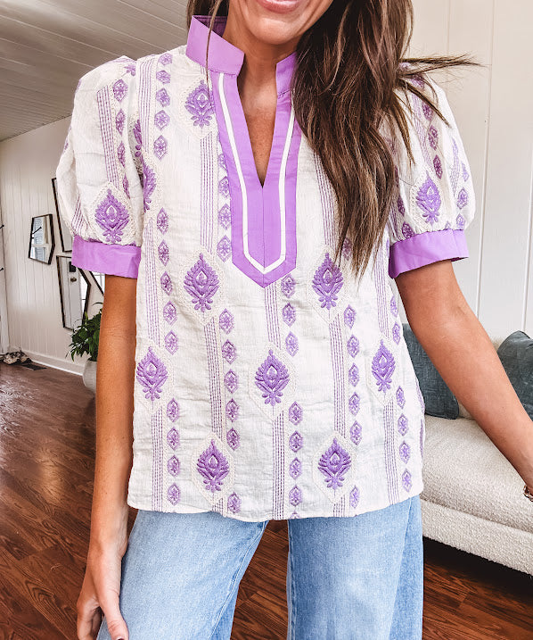 Fully lined lavender and cream blouse with lavender trim at the mock collar and V neck and cuffs, short puffed sleeves and lavender and cream embroidery throughout in an abstract pattern.
