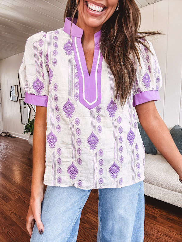 Fully lined lavender and cream blouse with lavender trim at the mock collar and V neck and cuffs, short puffed sleeves and lavender and cream embroidery throughout in an abstract pattern.