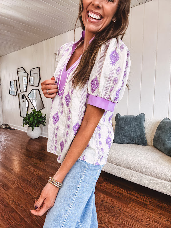 Fully lined lavender and cream blouse with lavender trim at the mock collar and V neck and cuffs, short puffed sleeves and lavender and cream embroidery throughout in an abstract pattern.