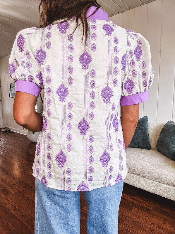 Fully lined lavender and cream blouse with lavender trim at the mock collar and V neck and cuffs, short puffed sleeves and lavender and cream embroidery throughout in an abstract pattern.