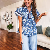 Lightweight cotton denim blue short sleeved top with mock neck and V neck design with shades of blue florals throughout and contrasting navy, white and light blue striping at the neckline and cuffs.