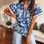 Lightweight cotton denim blue short sleeved top with mock neck and V neck design with shades of blue florals throughout and contrasting navy, white and light blue striping at the neckline and cuffs.