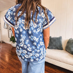 Lightweight cotton denim blue short sleeved top with mock neck and V neck design with shades of blue florals throughout and contrasting navy, white and light blue striping at the neckline and cuffs.