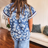 Lightweight cotton denim blue short sleeved top with mock neck and V neck design with shades of blue florals throughout and contrasting navy, white and light blue striping at the neckline and cuffs.