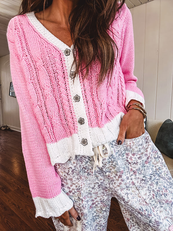 Light pink cable knit cardigan with white trim and flutter hem and cuffs with metal floral buttons down the front.