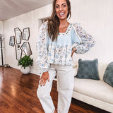 Light blue ribbed texture long sleeved top with sheer blue and green floral inserts at sleeves and ruffled hem with lace embroidery, elastic cuffs and round neck with lace and embroidery trim.