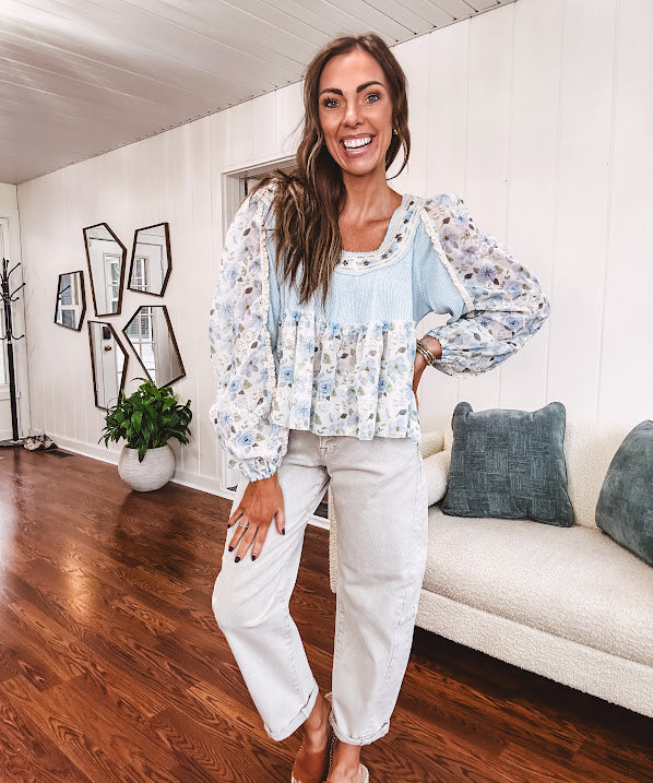 Light blue ribbed texture long sleeved top with sheer blue and green floral inserts at sleeves and ruffled hem with lace embroidery, elastic cuffs and round neck with lace and embroidery trim.
